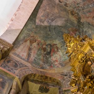 Pinturas murales renacentistas de San Pedro y el remate de un retablo barroco dorado bajo la bóveda románica.