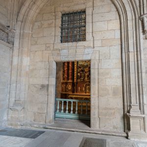 Entrada de piedra a la Capilla de Alba desde el claustro con lápidas en el suelo y vista al retablo barroco.