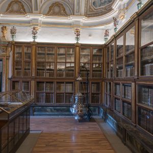 El Botafumeiro  expuesto en la Biblioteca Capitular sobre un soporte, rodeado de estanterías antiguas con libros históricos y decoración barroca.
