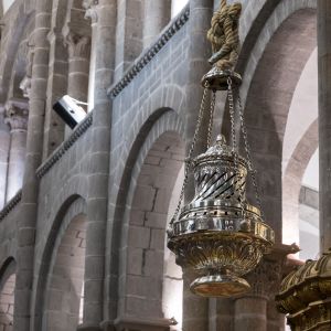 Primer plano del Botafumeiro de plata suspendido por una cuerda en el interior de la Catedral , mostrando detalles de su diseño y los arcos de piedra 