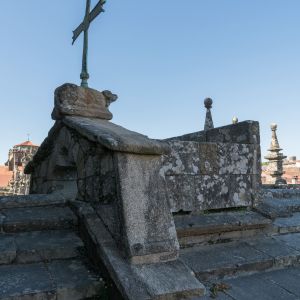 Cruz dos Farrapos sobre un pequeño conjunto de piedra en las cubiertas de la Catedral de Santiago, con un cordero simbólico y pináculos alrededor.