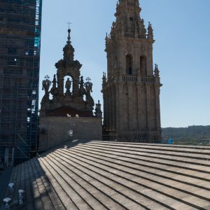 Cubiertas de losas escalonadas de la Catedral de Santiago con la peineta barroca del Obradoiro y la Torre de la Carraca al fondo, vista desde los teja
