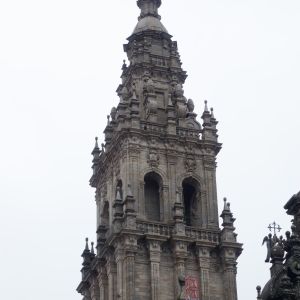 Detalle del remate barroco de la Torre de la Carraca en la Fachada del Obradoiro, con andamios de restauración y cielo despejado de fondo.