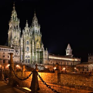 Vista nocturna de la fachada del Obradoiro iluminada, resaltando la Torre de las Campanas y la arquitectura barroca bajo el cielo oscuro.