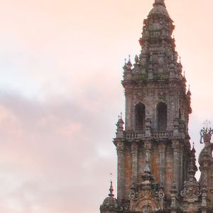 Detalle de la Torre de la Carraca de la Catedral de Santiago bajo un cielo rosado, mostrando sus cuerpos barrocos, balaustradas y pináculos.