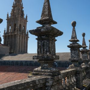 Primer plano de balaustrada con pináculos en las cubiertas de la Catedral de Santiago, con la Torre de la Carraca al fondo bajo un cielo despejado.